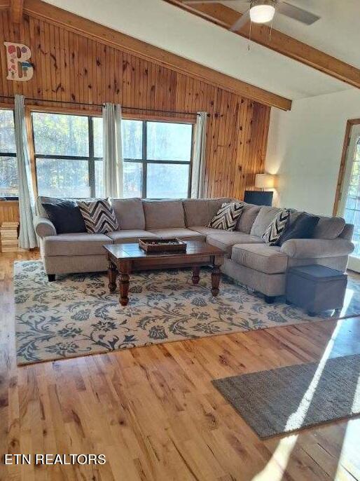 living room featuring ceiling fan, vaulted ceiling with beams, wood walls, and hardwood / wood-style flooring