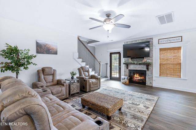 living room with ornamental molding, a fireplace, ceiling fan, and dark wood-type flooring