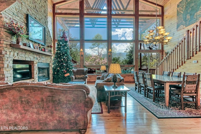 living room with high vaulted ceiling, a stone fireplace, hardwood / wood-style flooring, and wood walls