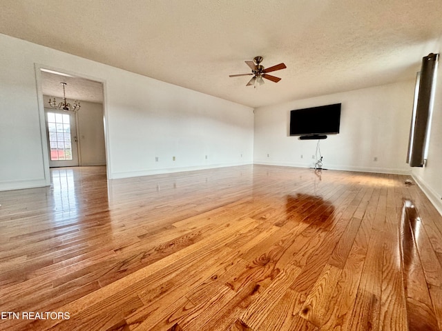 empty room featuring light hardwood / wood-style flooring, a textured ceiling, and ceiling fan with notable chandelier