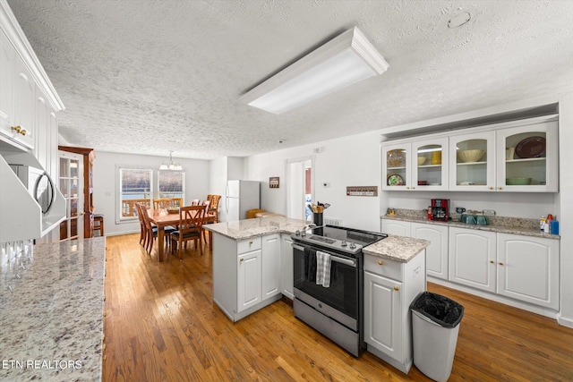 kitchen featuring light stone countertops, an inviting chandelier, light hardwood / wood-style flooring, white cabinets, and stainless steel electric stove