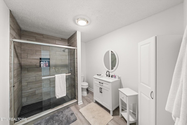 bathroom with toilet, hardwood / wood-style floors, a shower with shower door, a textured ceiling, and vanity