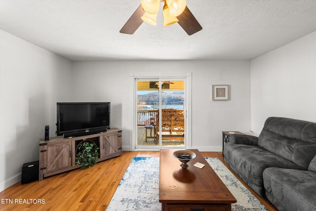 living room featuring ceiling fan, light wood-type flooring, and a textured ceiling