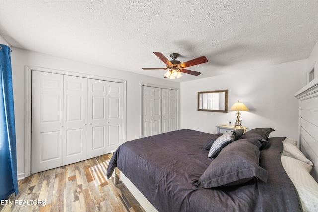 bedroom featuring multiple closets, a textured ceiling, ceiling fan, and light hardwood / wood-style flooring