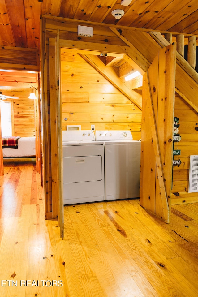 laundry room with wood ceiling, wooden walls, washing machine and clothes dryer, and light wood-type flooring