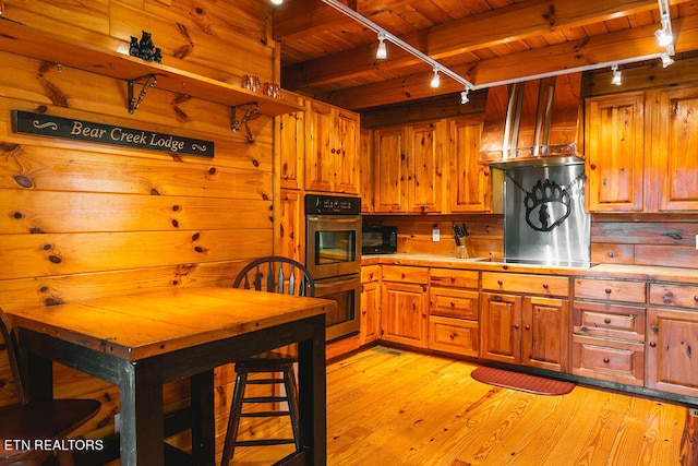 kitchen featuring wooden ceiling, track lighting, wooden walls, light hardwood / wood-style floors, and black appliances