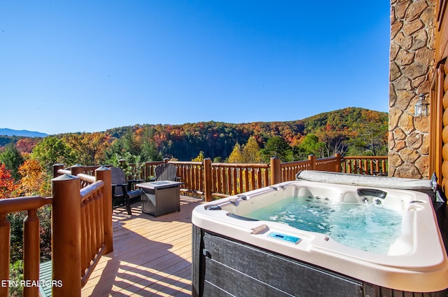 wooden terrace with a hot tub, a mountain view, and an outdoor fire pit