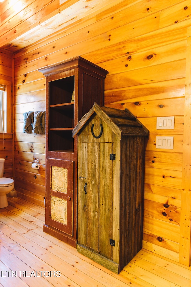 interior space featuring hardwood / wood-style flooring, wooden walls, and toilet