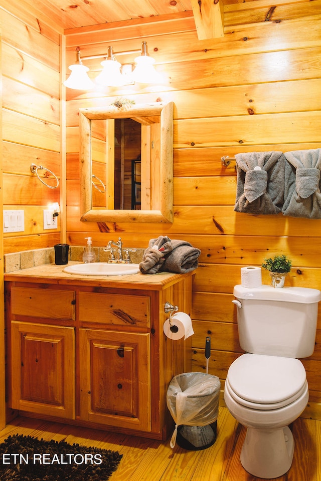 bathroom featuring vanity, wood-type flooring, wooden walls, and toilet