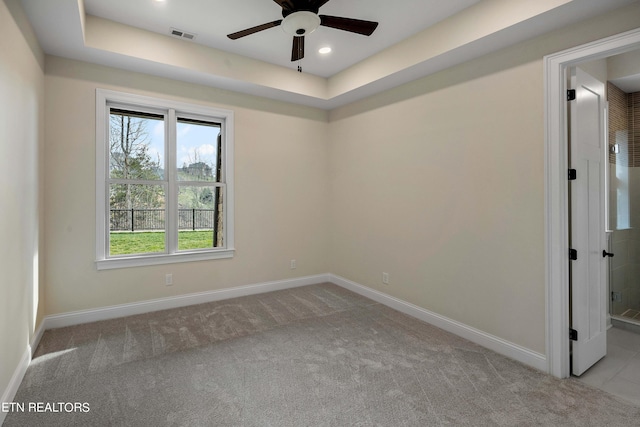 carpeted empty room with a raised ceiling and ceiling fan