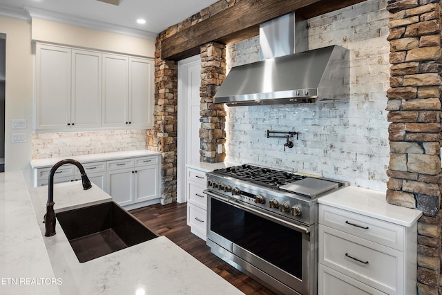 kitchen featuring wall chimney range hood, tasteful backsplash, white cabinets, high end stove, and sink