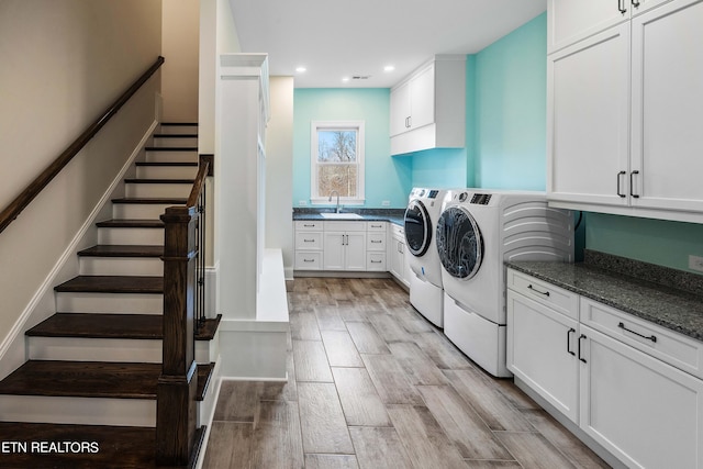 clothes washing area with washer and clothes dryer, light hardwood / wood-style floors, cabinets, and sink