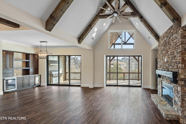 unfurnished living room featuring dark hardwood / wood-style flooring, a stone fireplace, high vaulted ceiling, ceiling fan with notable chandelier, and beam ceiling