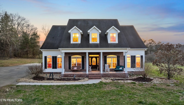 new england style home featuring a porch and a yard