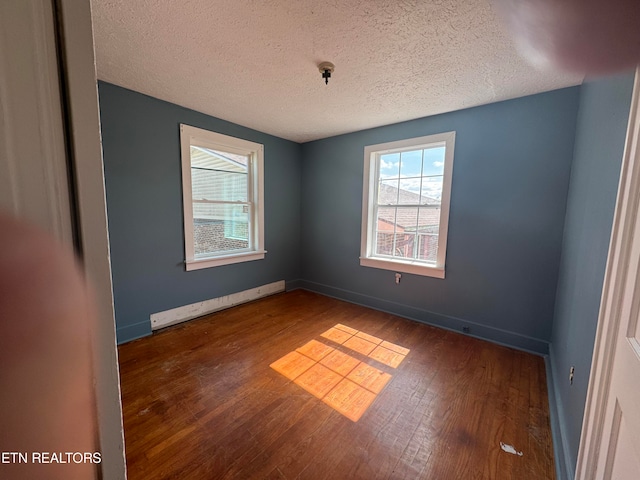 unfurnished room with hardwood / wood-style floors, a baseboard heating unit, and a textured ceiling