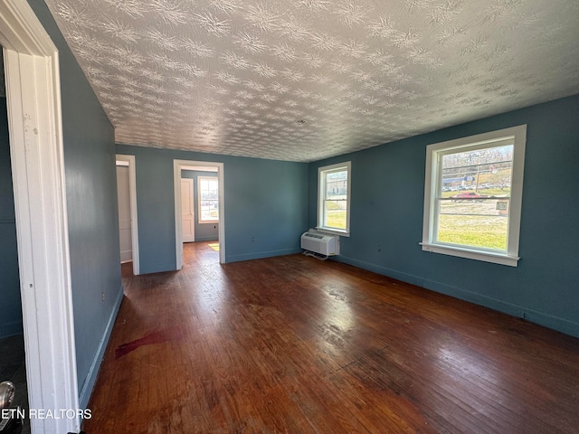 unfurnished room with a wall unit AC, a healthy amount of sunlight, a textured ceiling, and dark hardwood / wood-style flooring