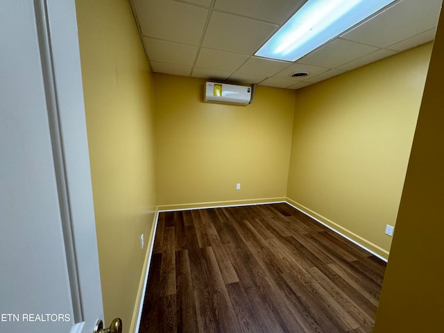 unfurnished room with a paneled ceiling, dark hardwood / wood-style floors, and a wall mounted air conditioner