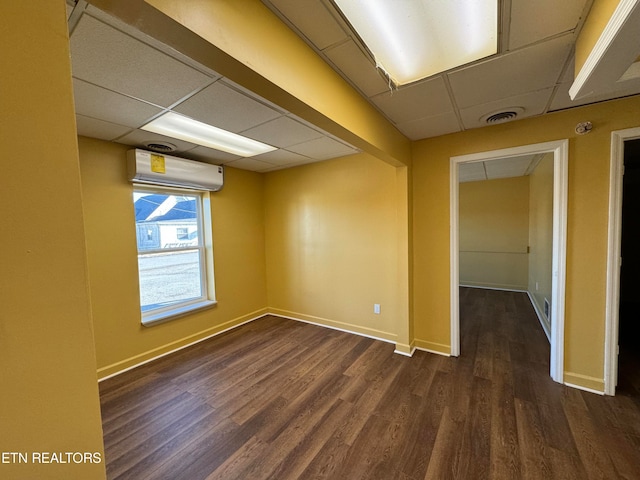 unfurnished room with a paneled ceiling, a wall mounted air conditioner, and dark hardwood / wood-style floors