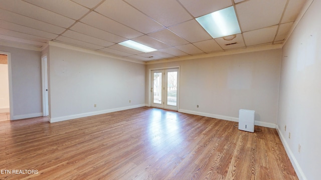 empty room featuring french doors, light hardwood / wood-style flooring, and a drop ceiling