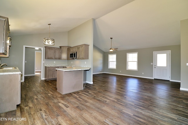 kitchen featuring hanging light fixtures, dark wood-type flooring, ceiling fan with notable chandelier, high vaulted ceiling, and light stone countertops