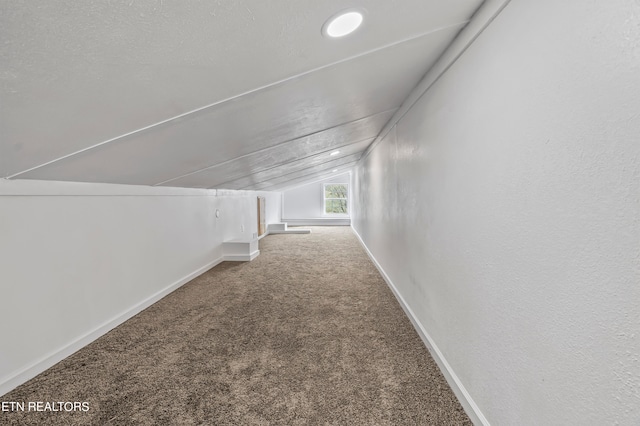 hallway with carpet flooring, vaulted ceiling, and a textured ceiling