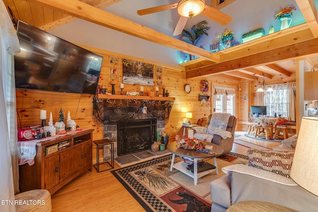 living room featuring ceiling fan, a fireplace, light hardwood / wood-style flooring, wood walls, and beam ceiling