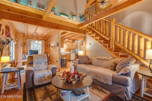 living room with beamed ceiling, wood walls, wood-type flooring, and ceiling fan with notable chandelier