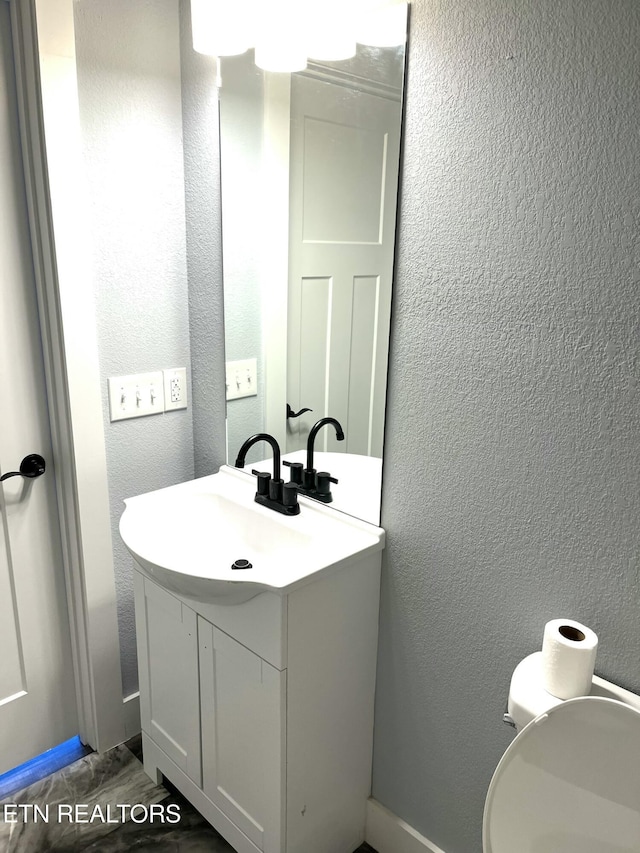 half bath featuring toilet, a textured wall, and vanity