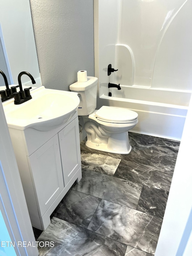 full bath with a textured wall, toilet, vanity, marble finish floor, and washtub / shower combination