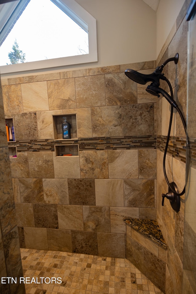 bathroom featuring lofted ceiling, a tile shower, and a healthy amount of sunlight