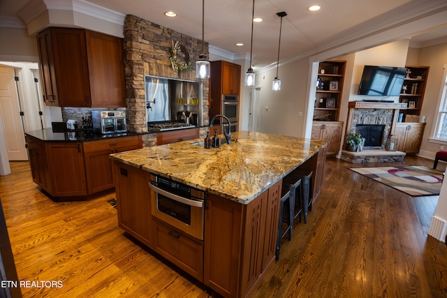 kitchen featuring dark stone counters, hardwood / wood-style floors, a fireplace, decorative light fixtures, and a center island with sink