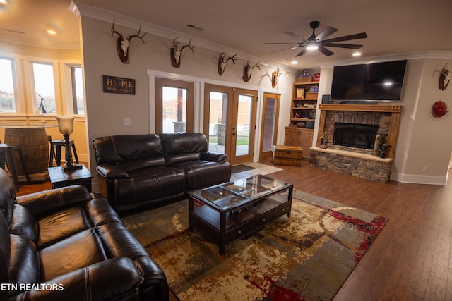 living room with a stone fireplace, built in features, crown molding, dark hardwood / wood-style floors, and ceiling fan