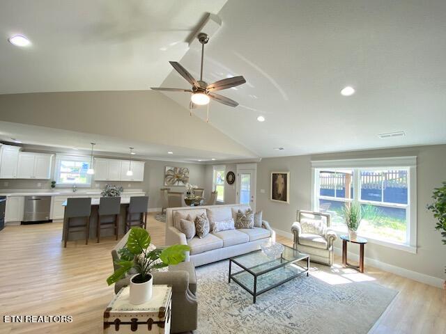 living room with light wood-type flooring, vaulted ceiling, ceiling fan, and sink