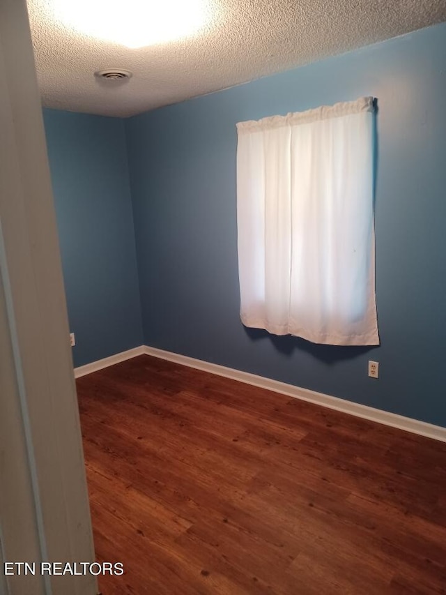 empty room featuring a textured ceiling and dark wood-type flooring