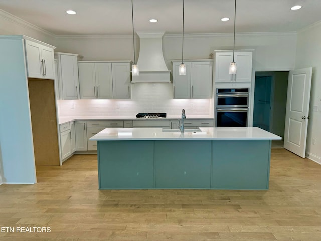 kitchen featuring white cabinetry, double oven, an island with sink, decorative light fixtures, and custom exhaust hood