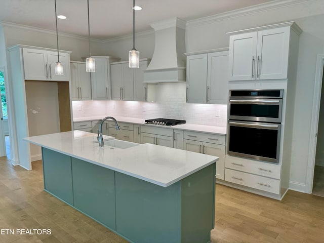 kitchen featuring sink, decorative light fixtures, custom range hood, and an island with sink