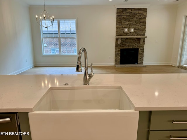 kitchen featuring sink, hanging light fixtures, a fireplace, ornamental molding, and light stone countertops