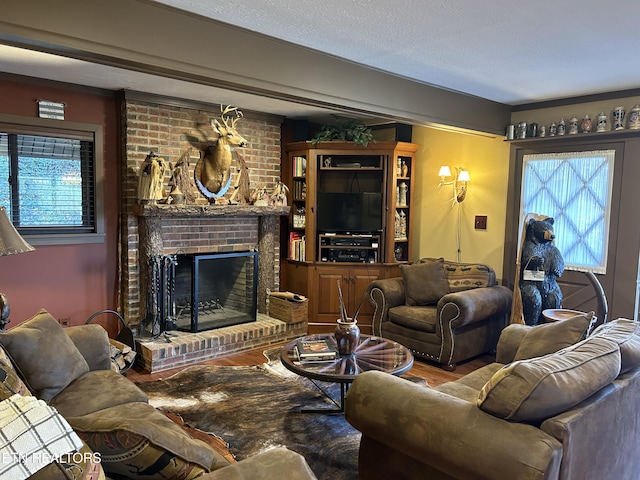 living room with a brick fireplace, brick wall, a textured ceiling, and hardwood / wood-style flooring