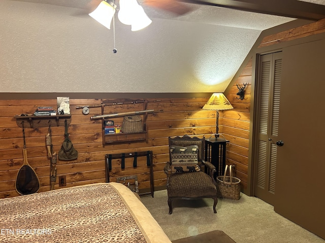 carpeted bedroom with wood walls, a closet, a textured ceiling, ceiling fan, and lofted ceiling