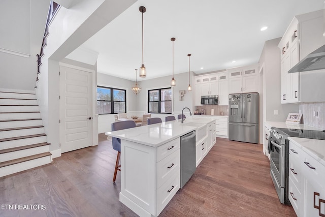 kitchen with appliances with stainless steel finishes, backsplash, an island with sink, and hardwood / wood-style flooring