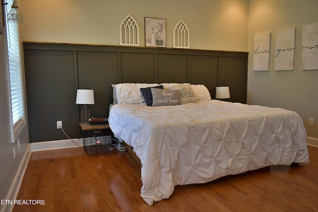 bedroom featuring a decorative wall, wood finished floors, and wainscoting