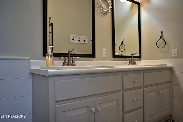 bathroom featuring wainscoting, a sink, tile walls, and double vanity