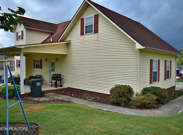 view of side of home with a yard, a shingled roof, and a patio area