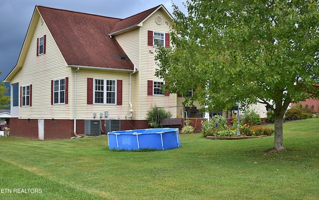 rear view of house with central air condition unit, a yard, and a covered pool