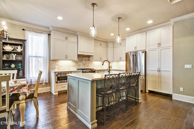 kitchen featuring stainless steel appliances, a center island with sink, dark hardwood / wood-style flooring, white cabinets, and pendant lighting