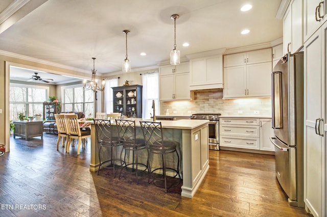 kitchen with appliances with stainless steel finishes, ceiling fan with notable chandelier, dark hardwood / wood-style floors, a kitchen island with sink, and pendant lighting