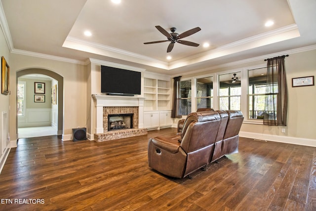 living room with ceiling fan, dark hardwood / wood-style floors, a brick fireplace, and a tray ceiling