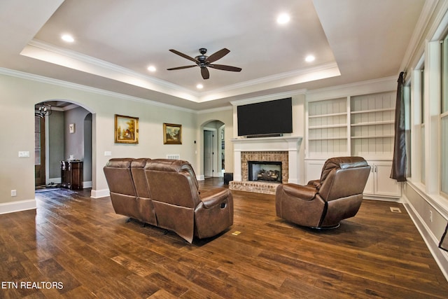 living room with crown molding, dark hardwood / wood-style flooring, a brick fireplace, and a raised ceiling