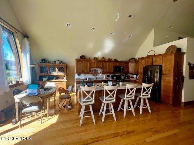 kitchen featuring black refrigerator, a breakfast bar, light hardwood / wood-style floors, high vaulted ceiling, and a center island