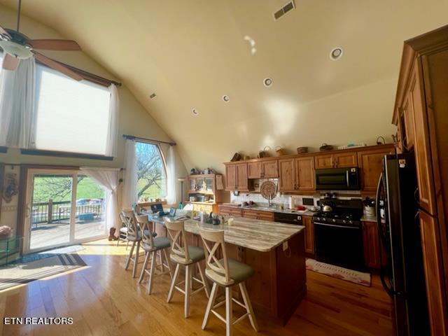 kitchen with range, black refrigerator, a center island, light wood-type flooring, and a kitchen breakfast bar